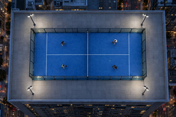 Una pista de pádel en la azotea de un edificio de una gran ciudad, vista desde arriba al anochecer, con cuatro jugadores. Imagen ilustrativa generada con IA; no es una foto del hecho.