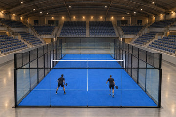Una pista de pádel montada en el centro de un pabellón cubierto, con las gradas vacías y dos jugadores de espaldas entrenando. Imagen ilustrativa generada con IA; no es una foto del hecho.